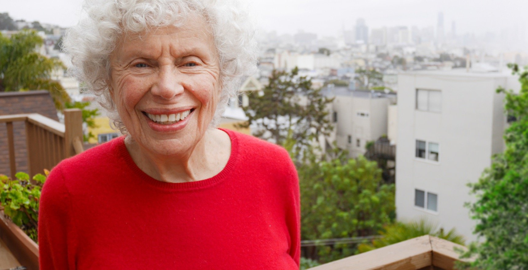 Aging woman stands on back patio overlooking city
